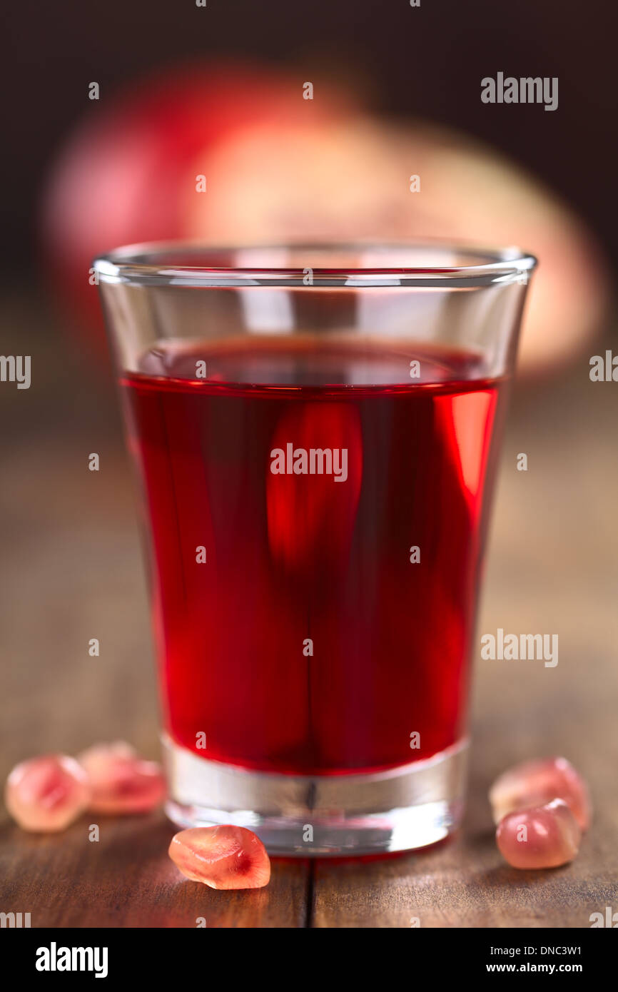 Grenadine syrup in shot glass with pomegranate seeds on the side and pomegranate in the back Stock Photo