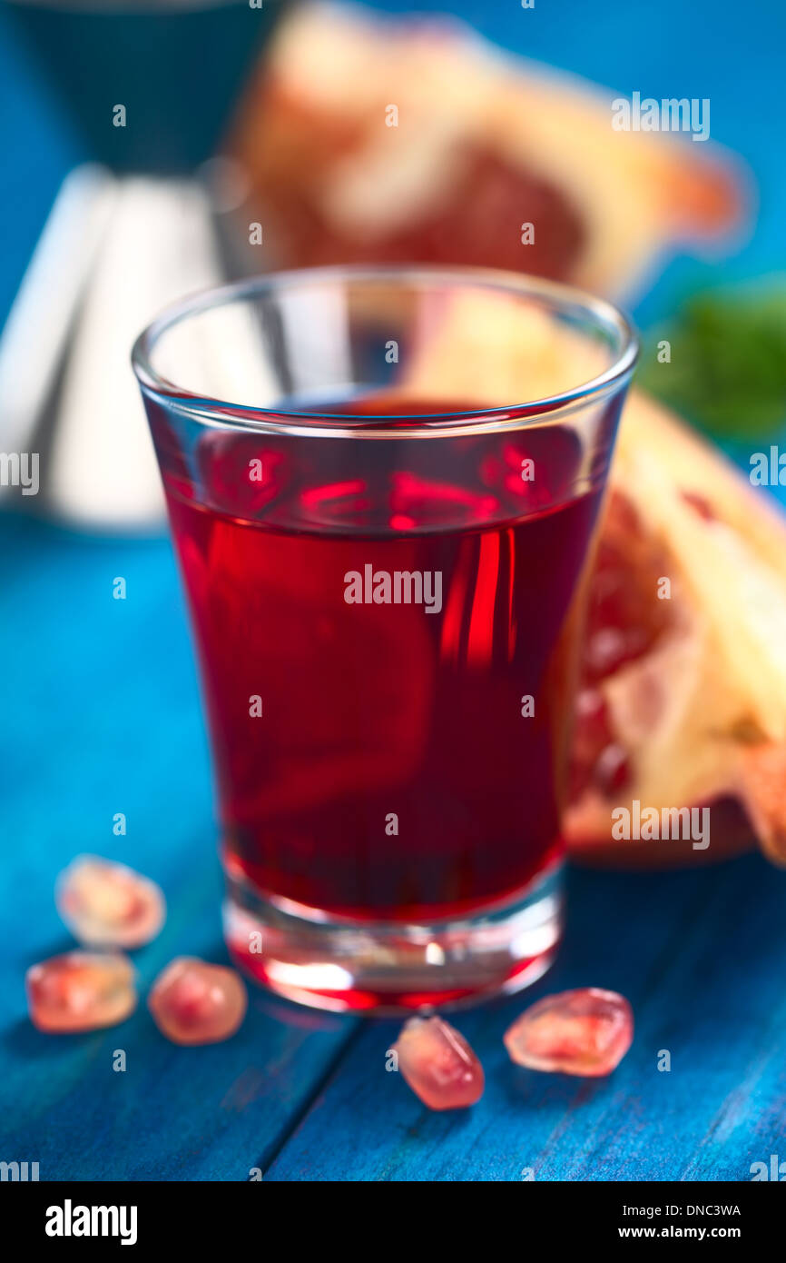 Grenadine syrup in shot glass with pomegranate seeds in the front and pomegranate in the back Stock Photo