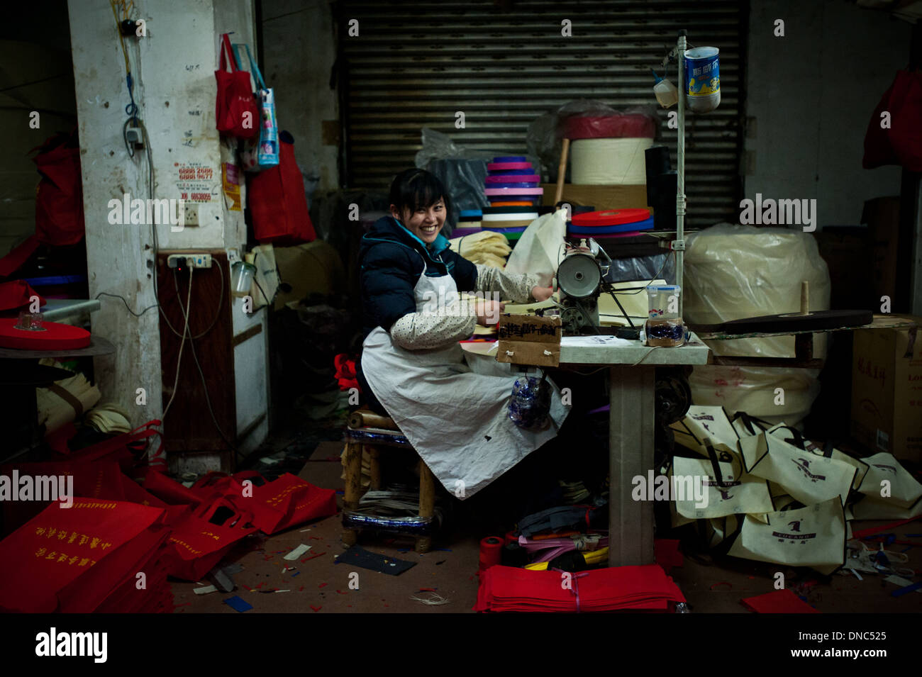 Chongqing, China - 31 December 2010: a woman smiles at the camera while working on a sewing machine in a messy textile factory Stock Photo