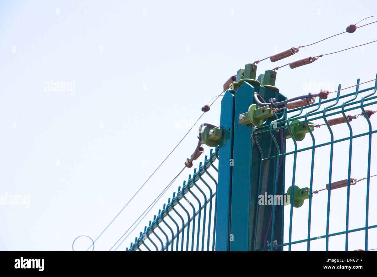 blue and green electric fence against pale blue sky Stock Photo - Alamy