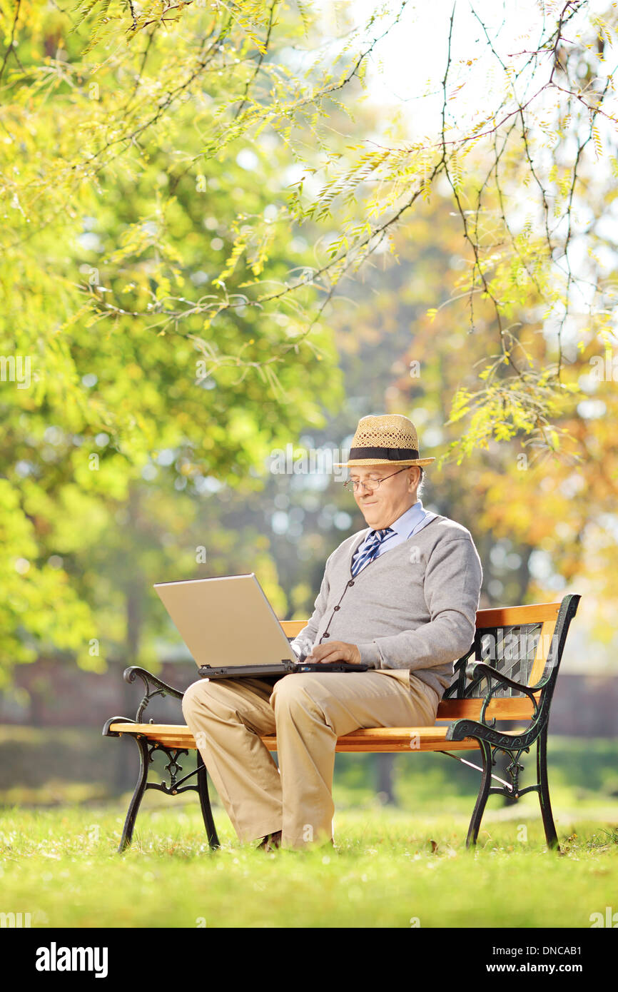 Senior man on a bench and working on a laptop in a park Stock Photo