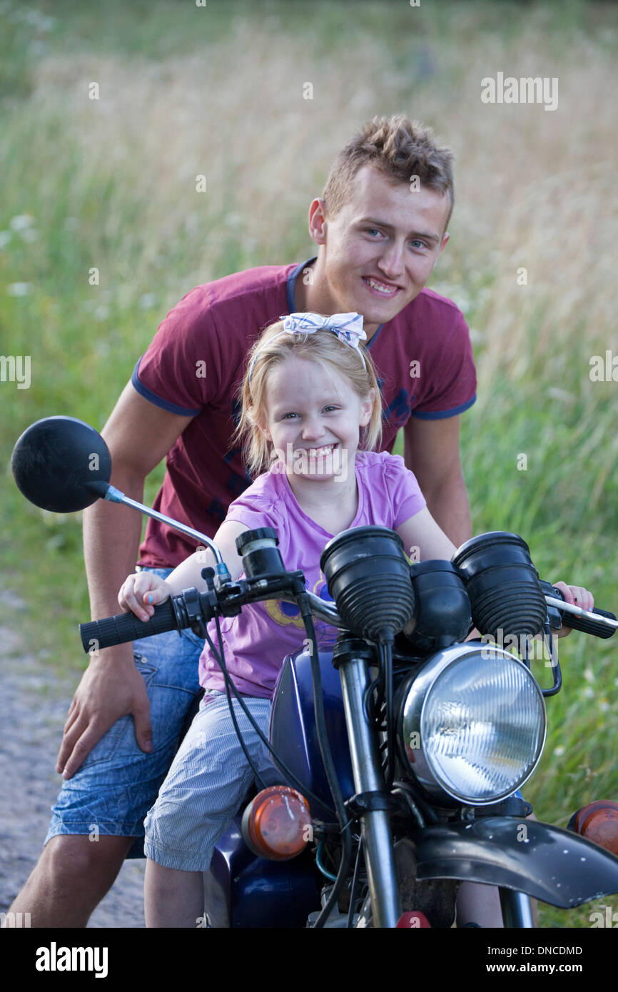 Polish teen boy motorcyclist giving ride to excited neighbor girl age 18 and 5. Zawady Central Poland Stock Photo