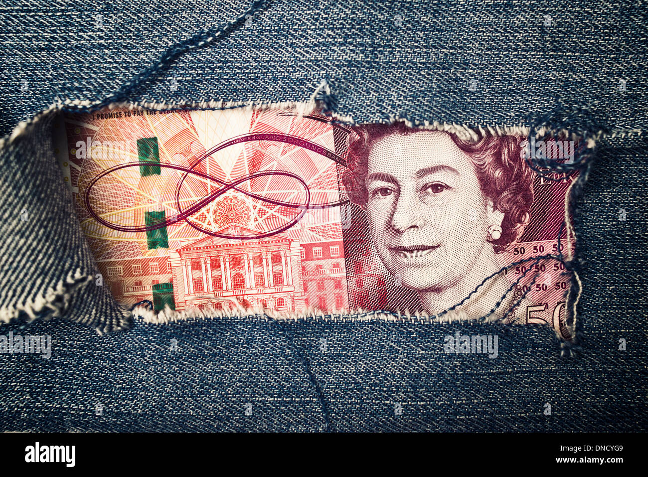 Fifty pounds bill through torn blue jeans texture. British economy concept. Stock Photo