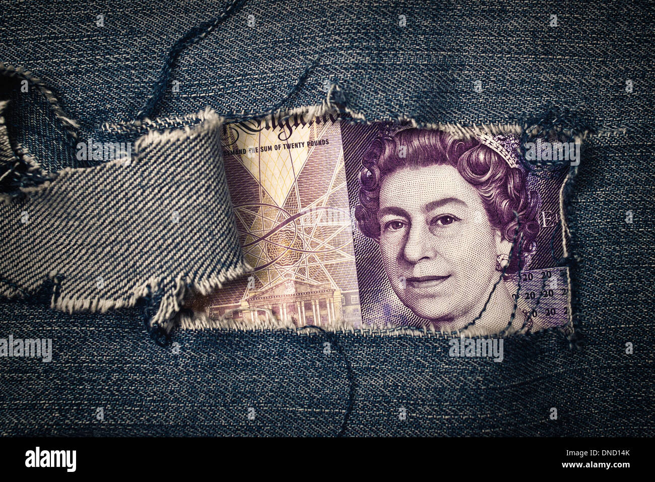 Twenty pounds bill through torn blue jeans texture. British economy concept. Stock Photo