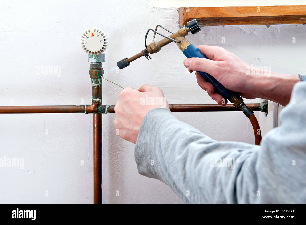 Plumber using welding gas torch to solder copper central heating pipes
