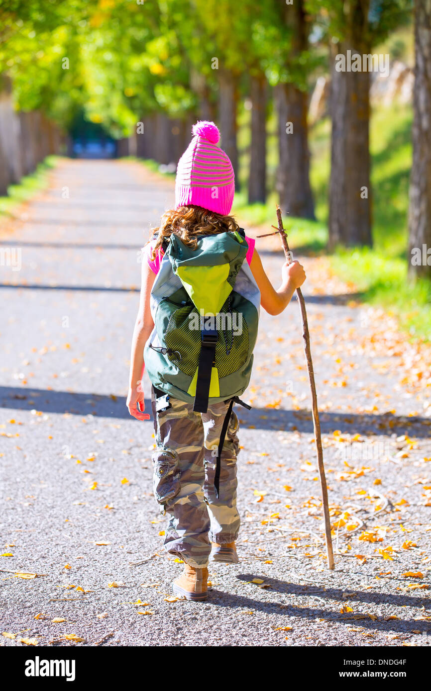 hiking kid girl with walking stick and backpack rear view at autumn track and camouflage pants Stock Photo