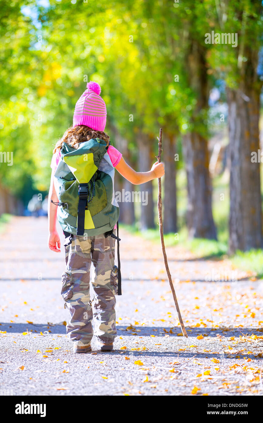 hiking kid girl with walking stick and backpack rear view at autumn track and camouflage pants Stock Photo