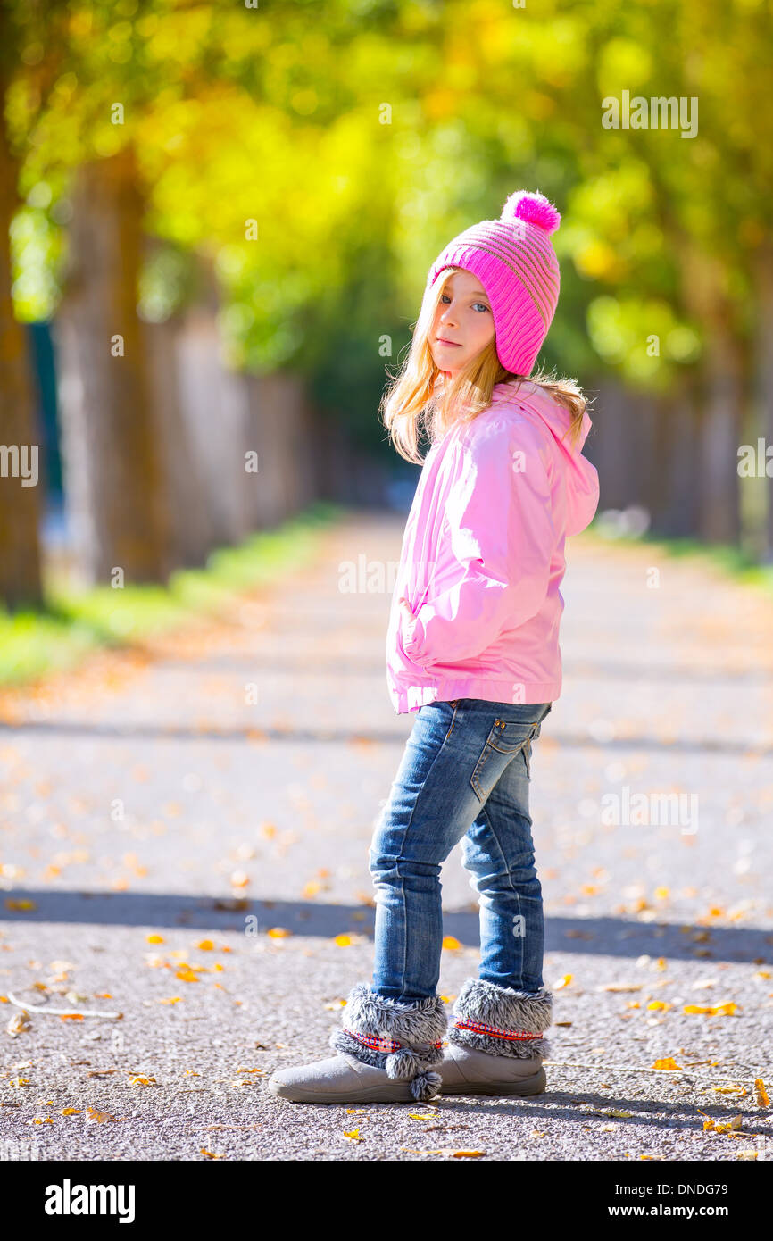 autumn winter kid girl blond with jeans and pink snow cap in trees track Stock Photo