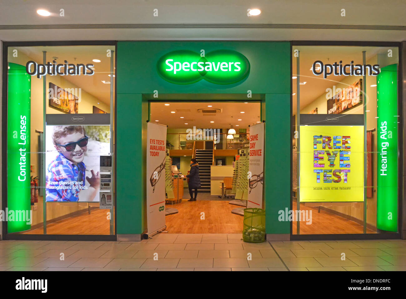 Customer inside Specsavers Opticians shop front doors open store window poster free eye test Lakeside shopping centre mall Thurrock Essex England UK Stock Photo