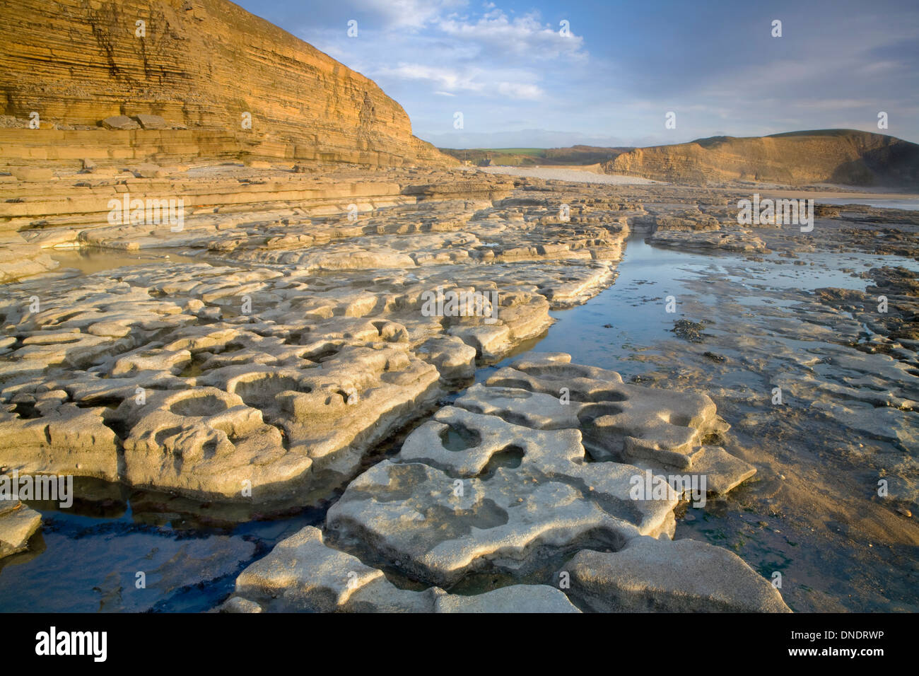Rock formations at Dunraven Bay, South Wales, are caused by the power of the sea. The setting sun lights up the headland cliffs. Stock Photo