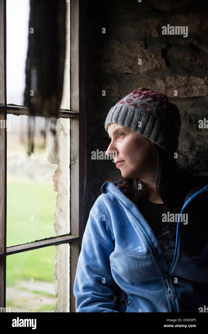 Female hiker looks out window of Burnmouth Bothy, Rackwick Bay, Hoy, Orkney, Scotland Stock Photo