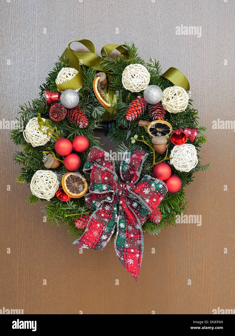 Christmas wreath with decorations and ribbon bow attached to the wooden door Stock Photo