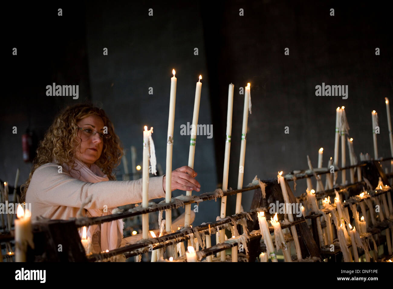 A woman lights a candle in the votive room of the Sanctuary of Our Lady of Rocio in El Rocio village, Andalusia, Spain Stock Photo