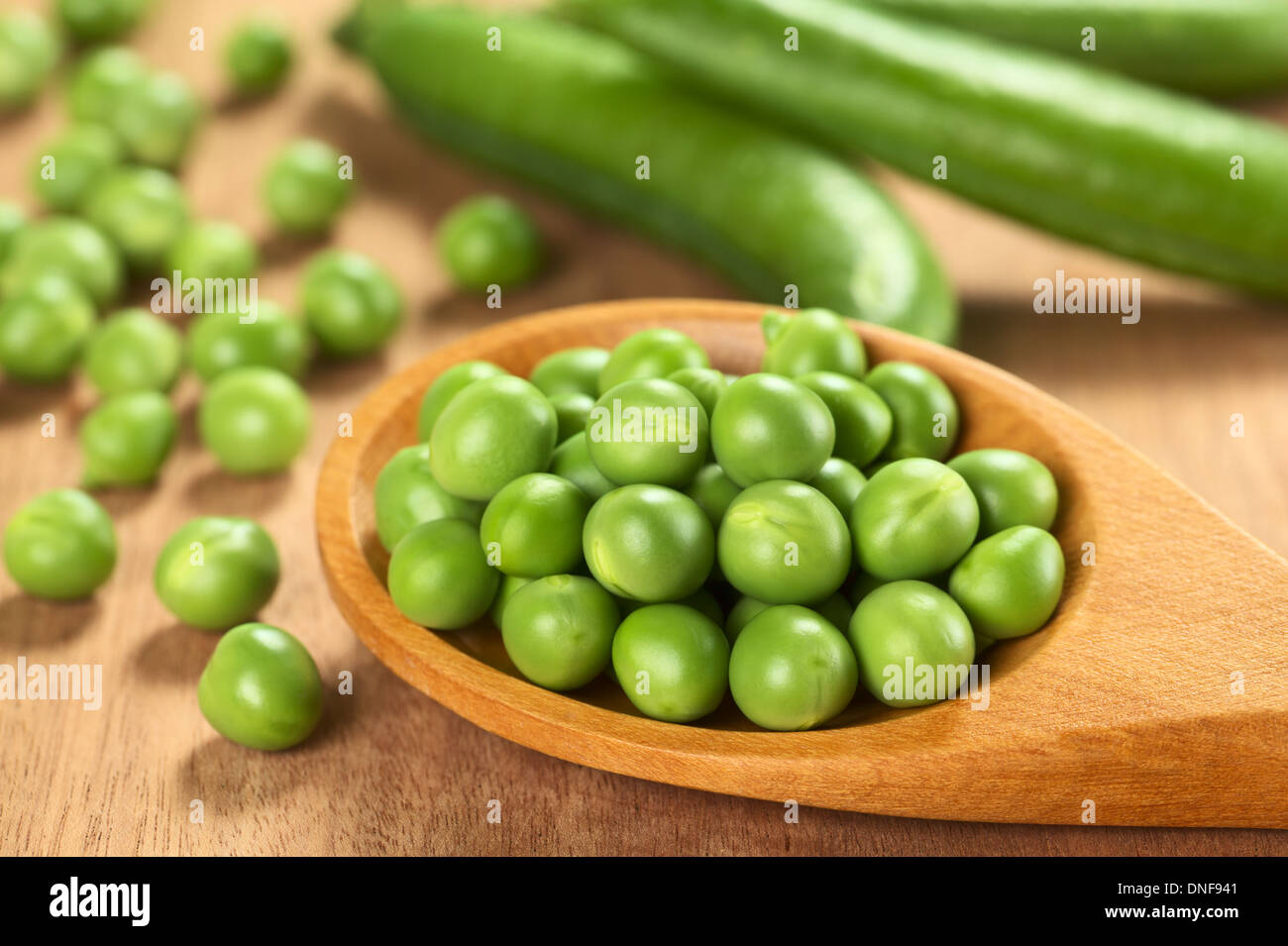 Fresh raw green pea (lat. Pisum Sativum) seeds on wooden spoon (Selective Focus, Focus on the peas in the two lower rows) Stock Photo
