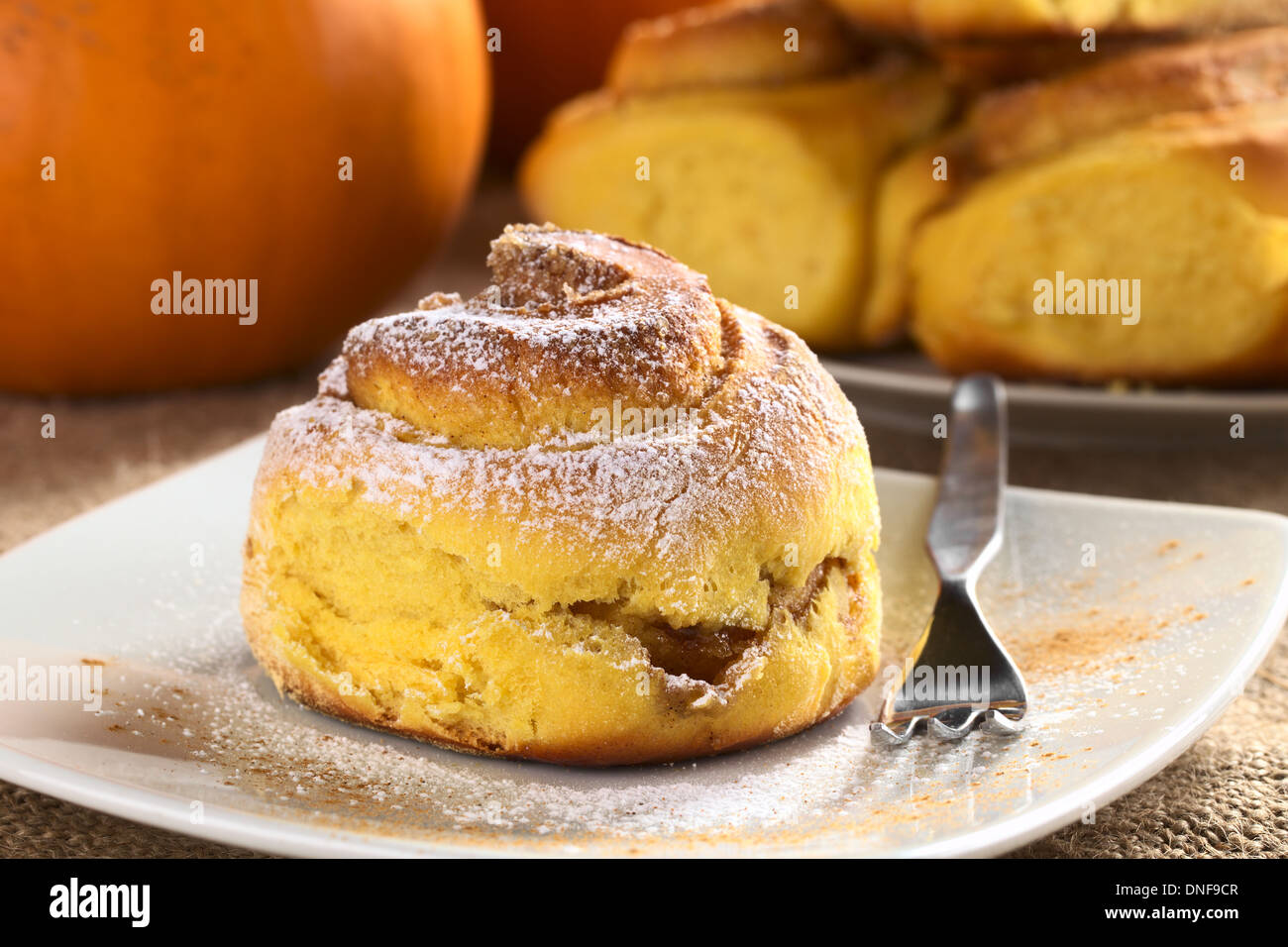 Pumpkin cinnamon roll with pumpkin and a plate full of rolls in the back Stock Photo