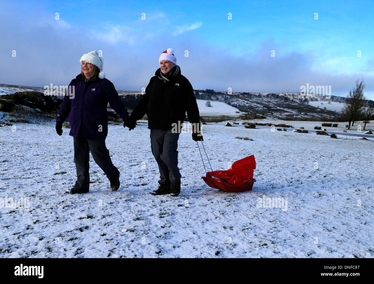 Buxton, Derbyshire, UK. 25th Dec, 2013.  After waking up to a white Christmas, Colin Chandler and Judith Irwin use a sledge to deliver Christmas presents on Christmas Day in Buxton in the Derbyshire Peak District. Credit:  Joanne Roberts/Alamy Live News Stock Photo