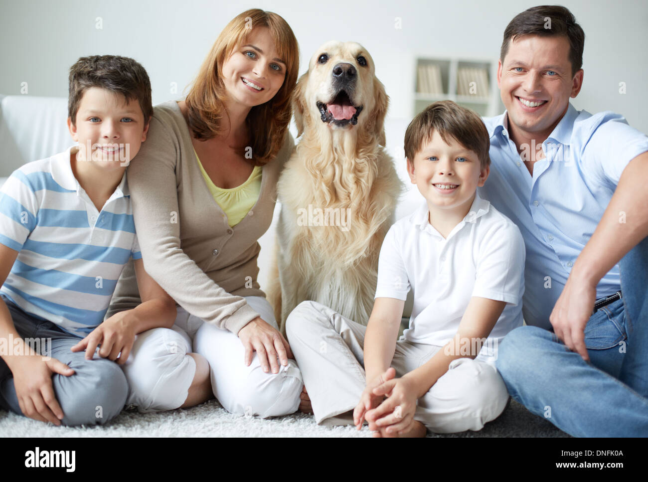 Portrait of happy family with fluffy Labrador having rest at home Stock