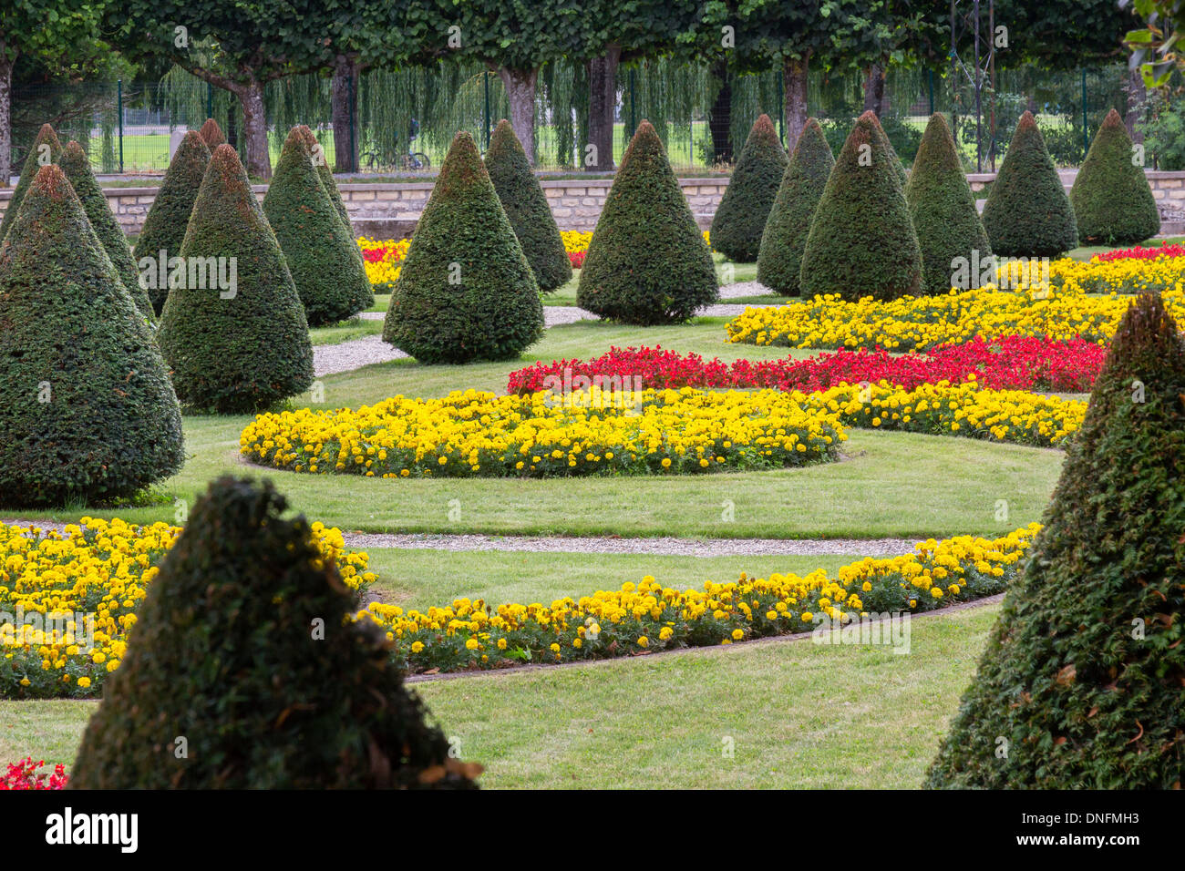 Clipped yew cones and flowerbeds with red begonias, yellow French marigolds, garden of Buzançais Hospital (Indre, France) Stock Photo