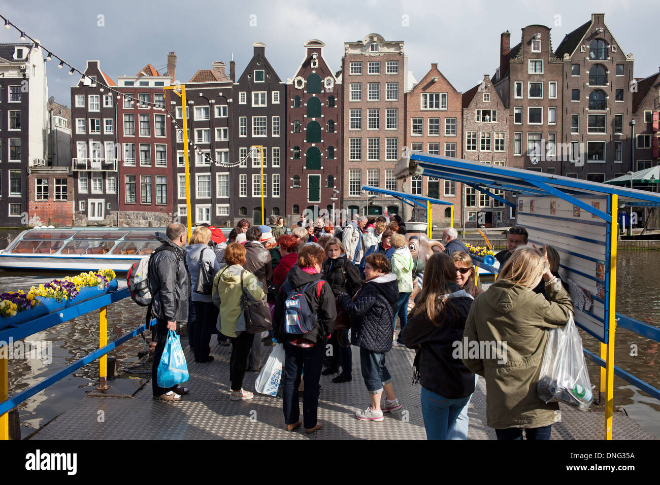 Group of tourists waiting at a canal boat tours pier in the Old Town of Amsterdam, Holland, the Netherlands. Stock Photo