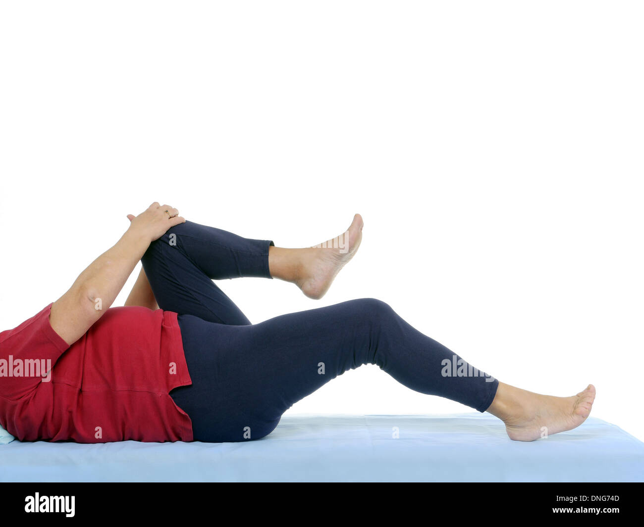 Older patient performing functional test of hip joint contraction lying on bed Stock Photo