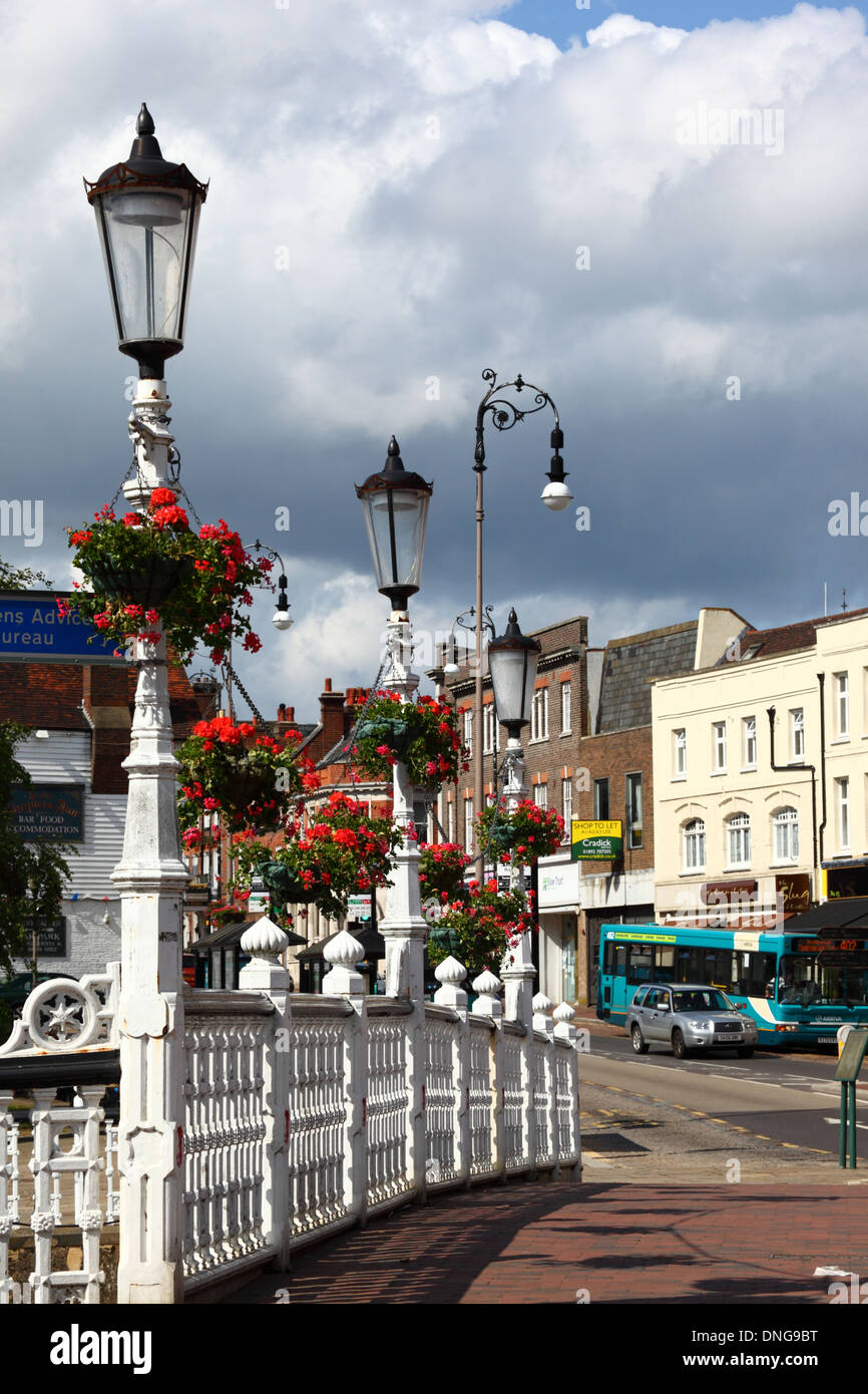 View along High Street, railings of bridge over River Medway and geraniums in hanging baskets on street lamps in foreground, Tonbridge, Kent, England Stock Photo