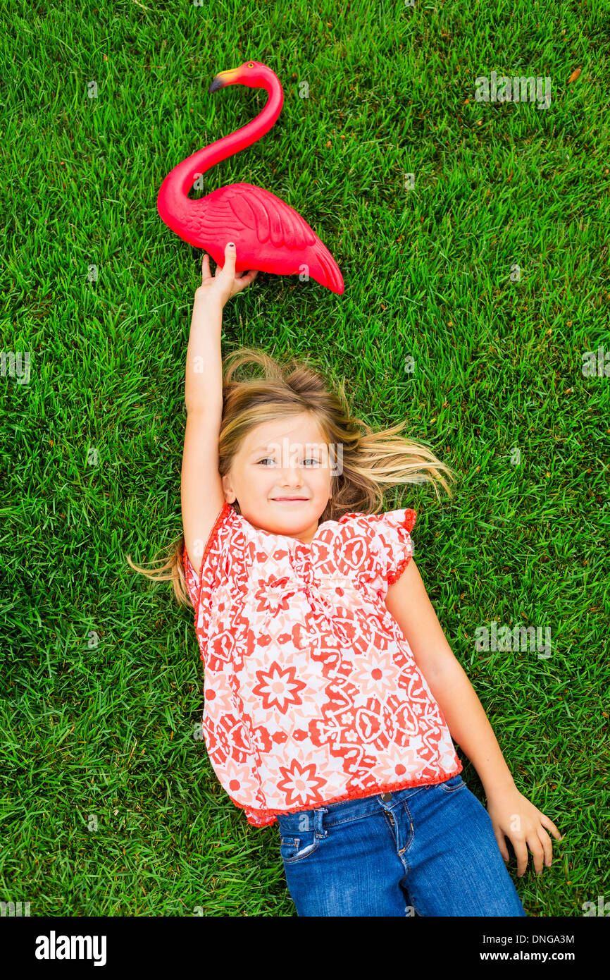Cute happy little girl smiling outside dying on the grass with flamingo ...