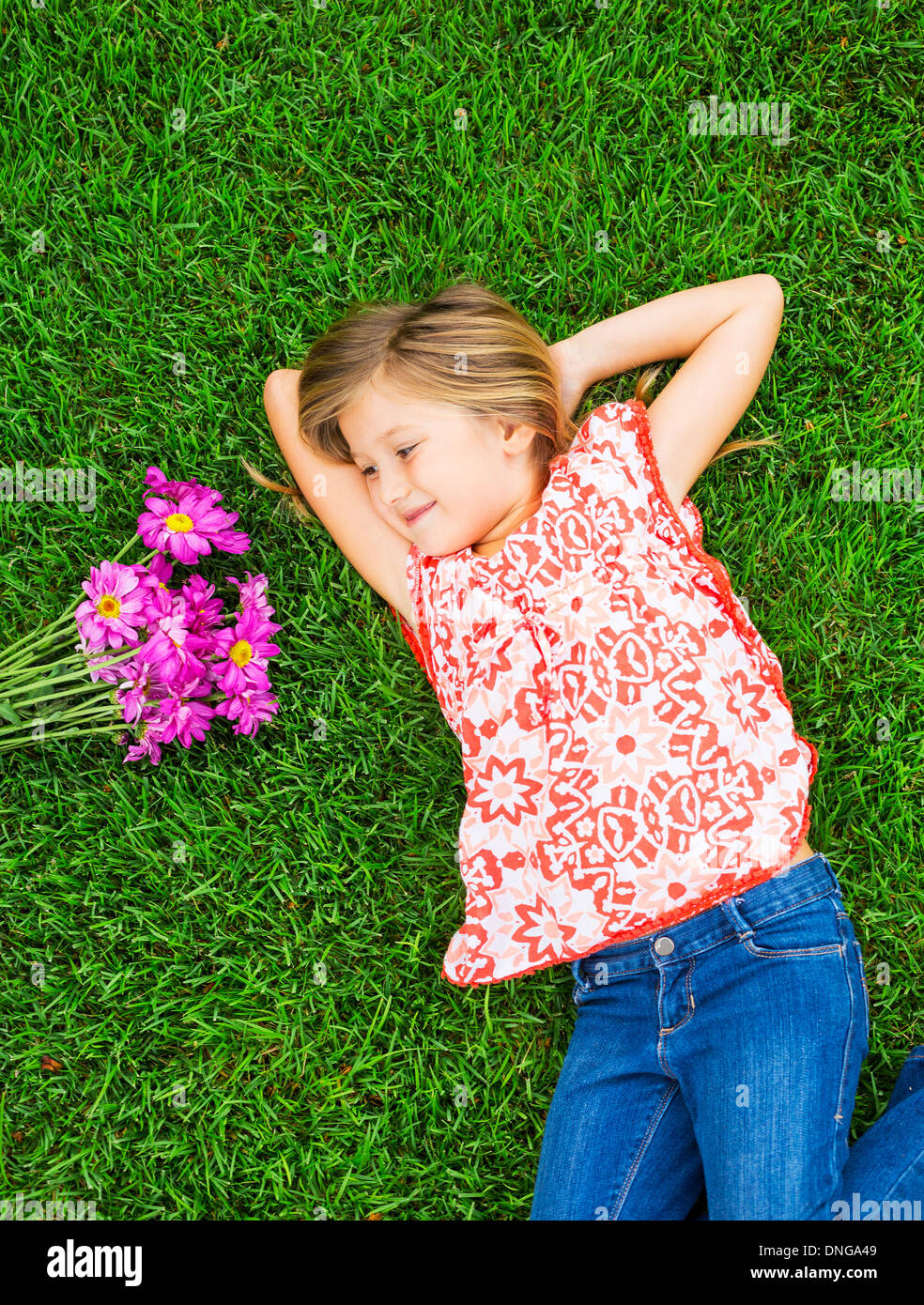Cute happy little girl smiling outside lying on the grass with flowers ...