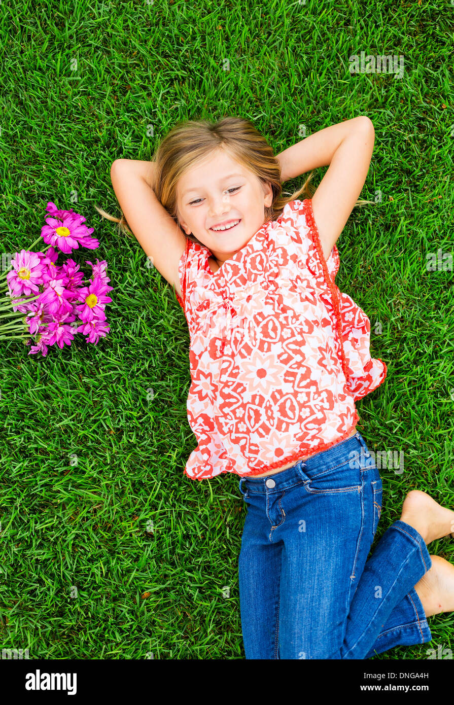 Cute happy little girl smiling outside lying on the grass with flowers ...