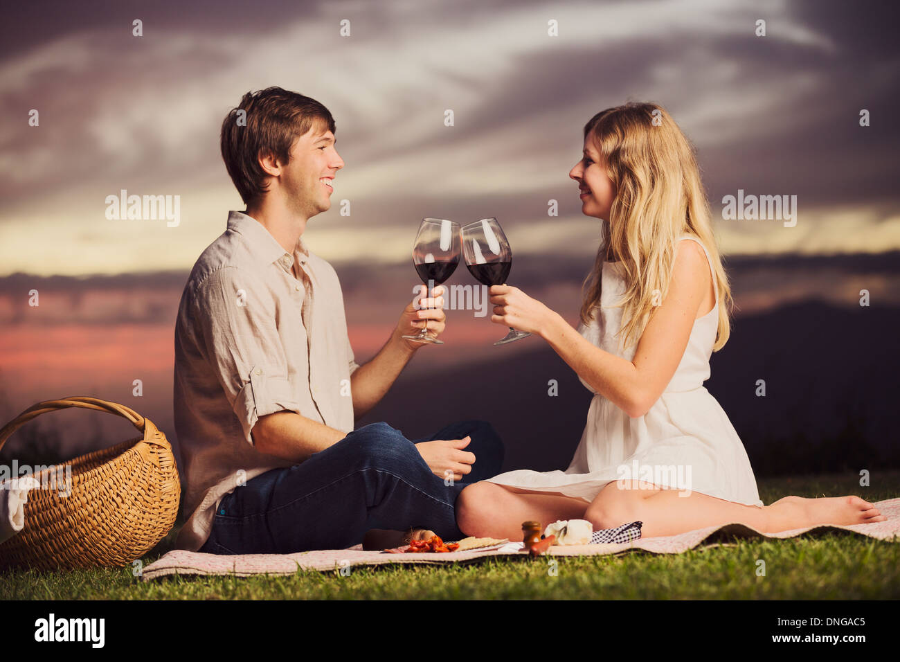 Attractive couple drinking glass of wine on romantic sunset picnic ...