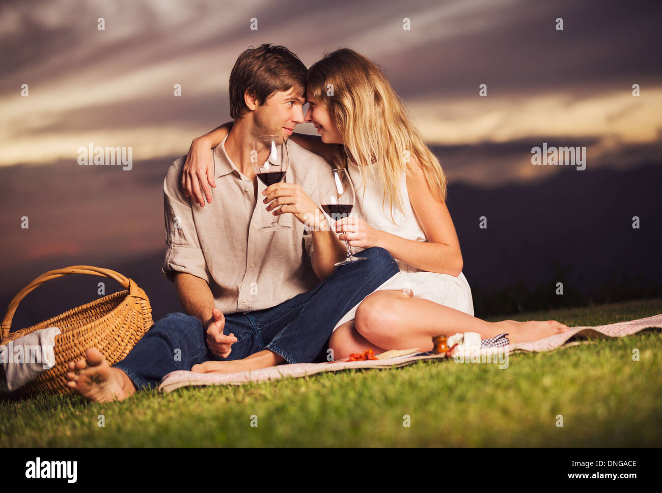 Attractive couple drinking glass of wine on romantic sunset picnic ...