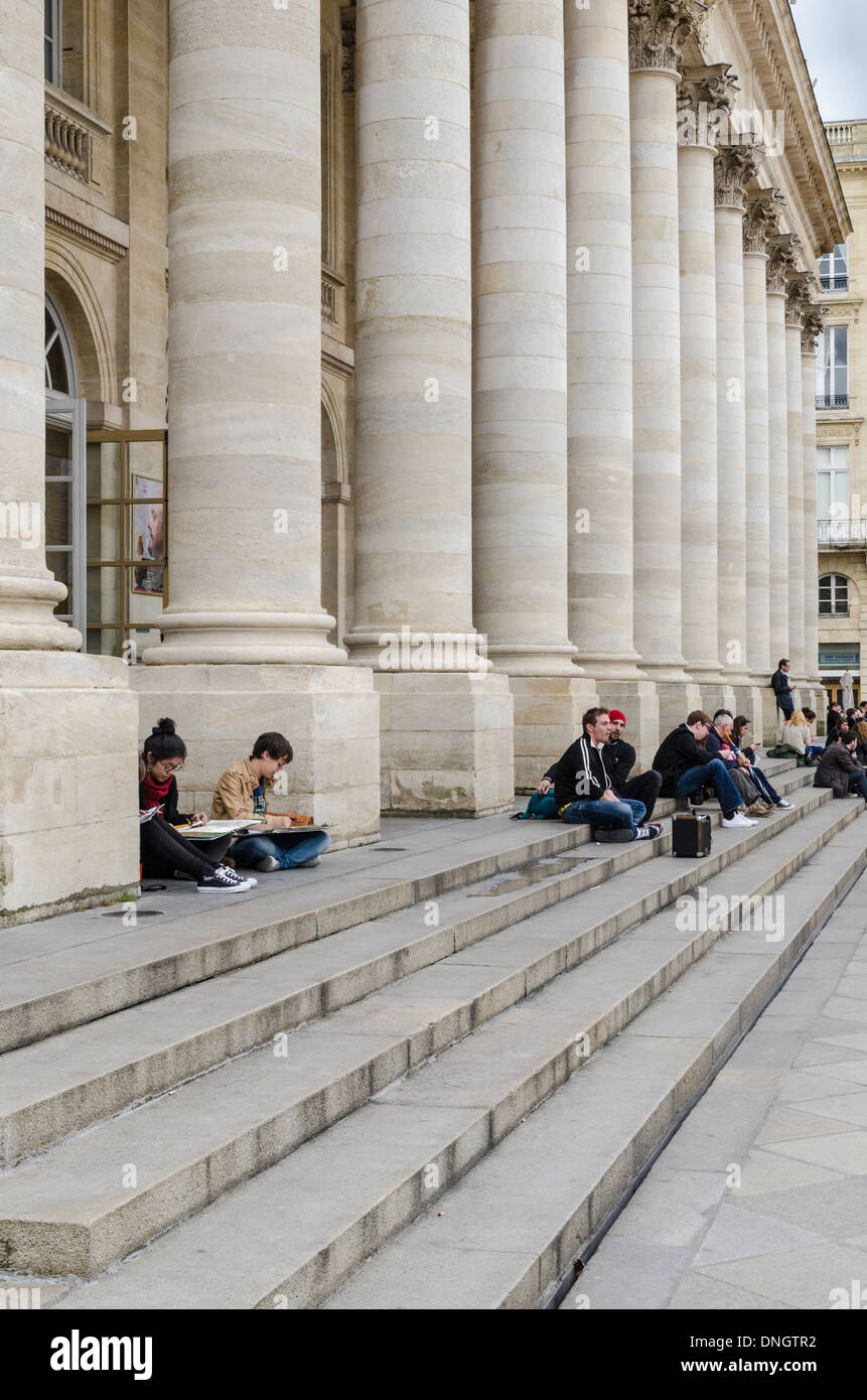 Students sitting on the steps of the Grand Theatre de Bordeaux, home of Opera National de Bordeaux, Place de la Comedie, France Stock Photo