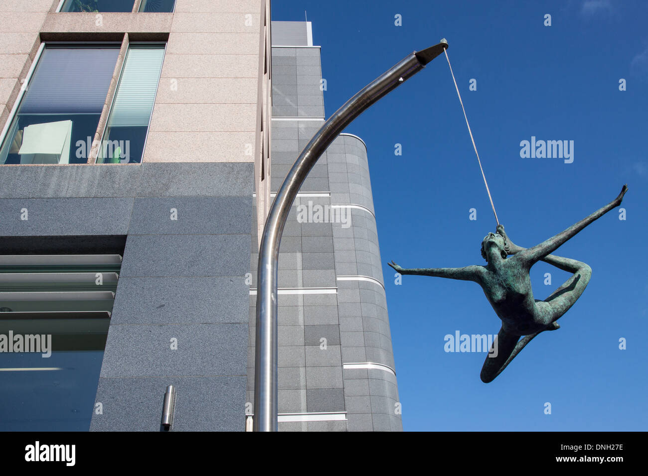 JERSEY GIRL, CONTEMPORARY STATUE HANGING FROM A CABLE AND MOVING IN THE WIND, IN FRONT OF AN OFFICE BUILDING, TOWN CENTRE OF SAINT HELIER, JERSEY, CHANNEL ISLANDS Stock Photo