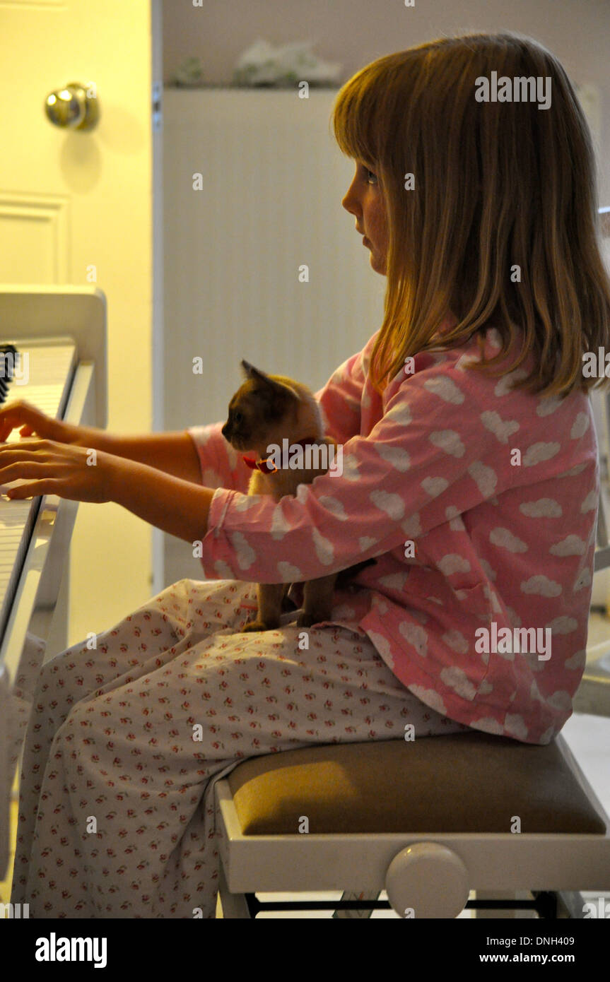 portrait of little girl playing the piano with a burmese kitten cat sitting on her lap as she plays Stock Photo