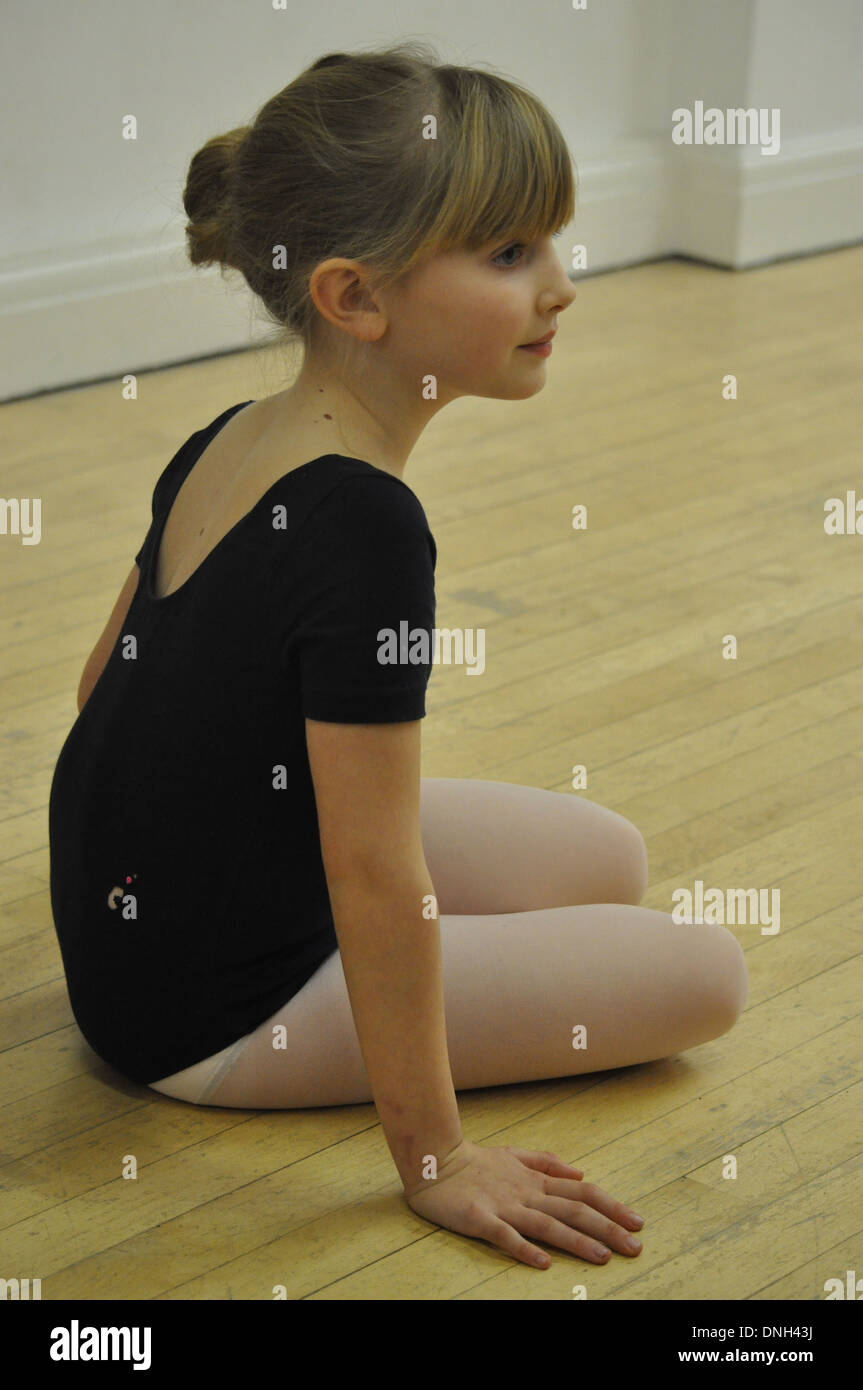 a little blonde girl in blue leotard sits down during her ballet class Stock Photo