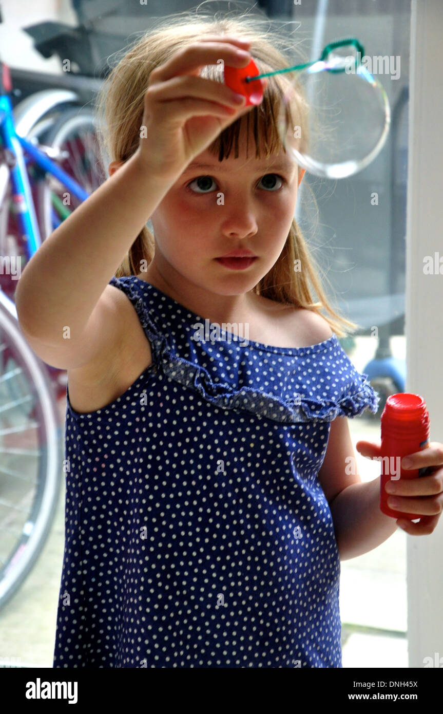 little blonde girl watches a bubble forming as she blows bubbles Stock Photo