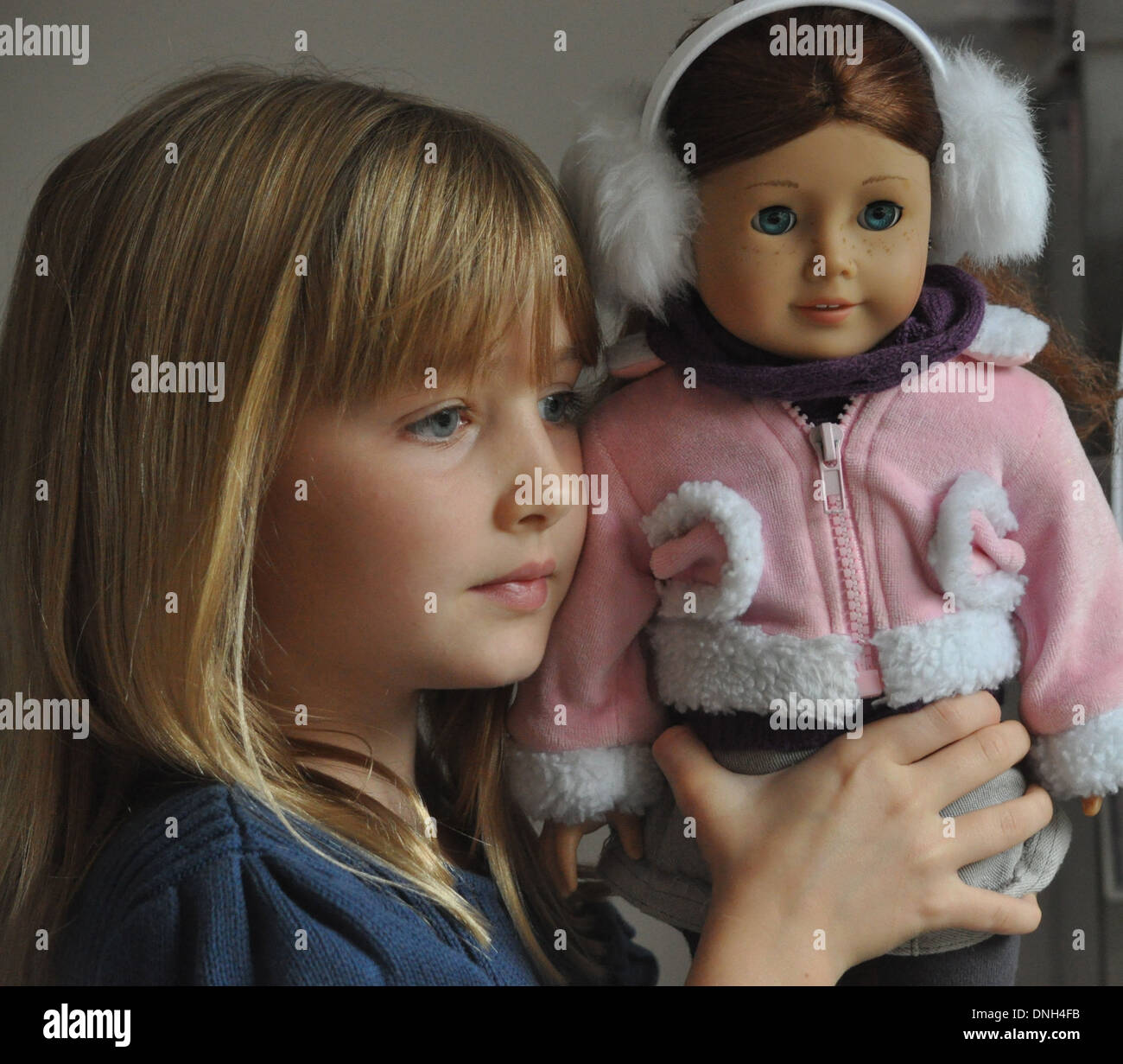 portrait of pretty blonde girl holding doll and looking out of window Stock Photo