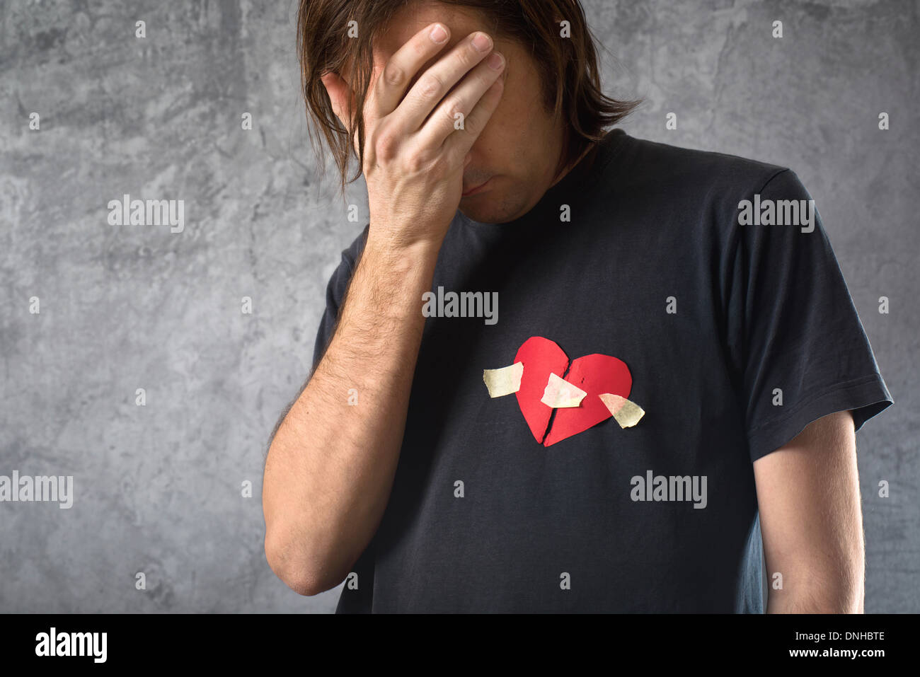 Broken hearted man is crying. Valentines day concept. Broken heart taped to his shirt. Stock Photo