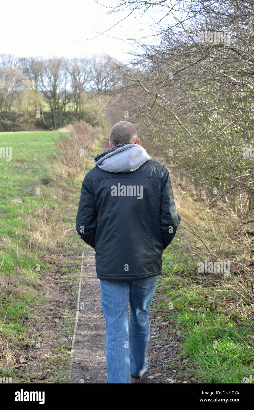 Man in hooded jacket walking down country path Stock Photo