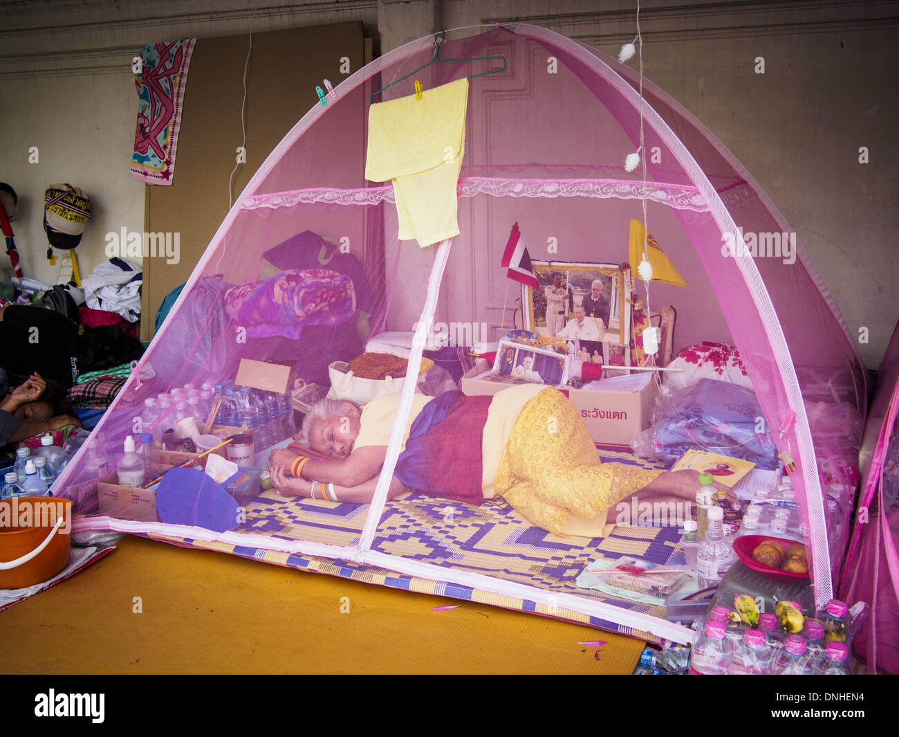 Bangkok, Thailand. 30th Dec, 2013. A woman sleeps in her tent at the anti-government protest site near Government House in Bangkok. She is wearing yellow, the color of the Thai monarchy, and has a picture of Bhumibol Adulyadej, the King of Thailand, in her tent. Most of the protestors are ultra monarchists. Violence around the anti-government protest sites has escalated in recent days and several protestors have been hurt by small explosive devices thrown at their guard posts. As a result, protestors are fortifying their positions with sandbags and bunkers. Credit:  ZUMA Press, Inc./Alamy Live Stock Photo