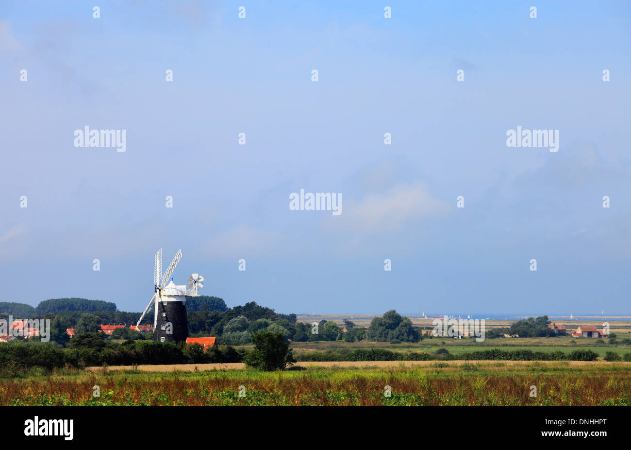 The windmill at Burnham Overy on the Norfolk coast with boats in the sea and marshland behind. Stock Photo