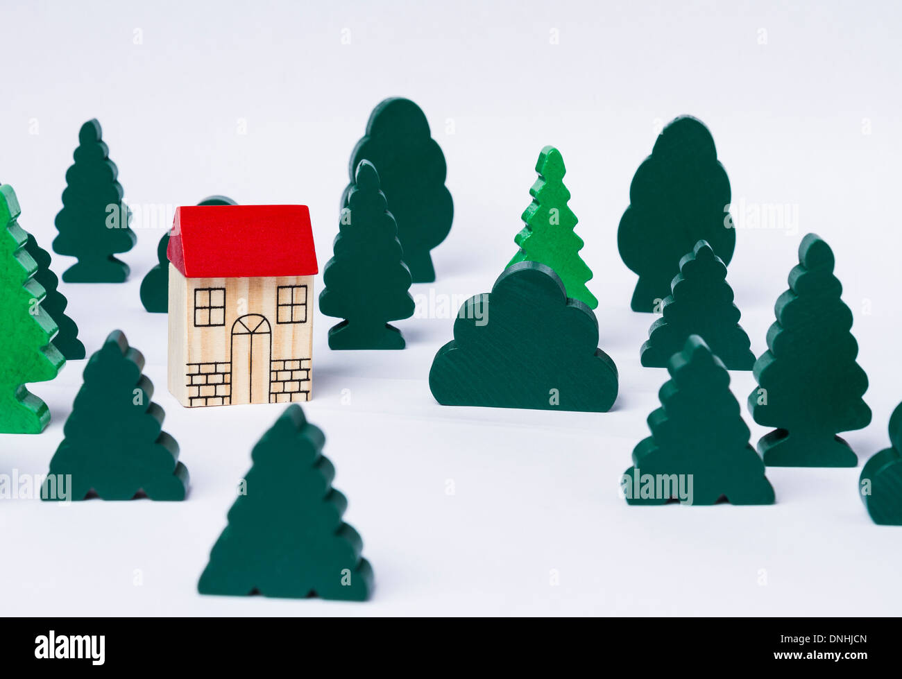 simple toy house in forest made of several trees. Grey background Stock Photo