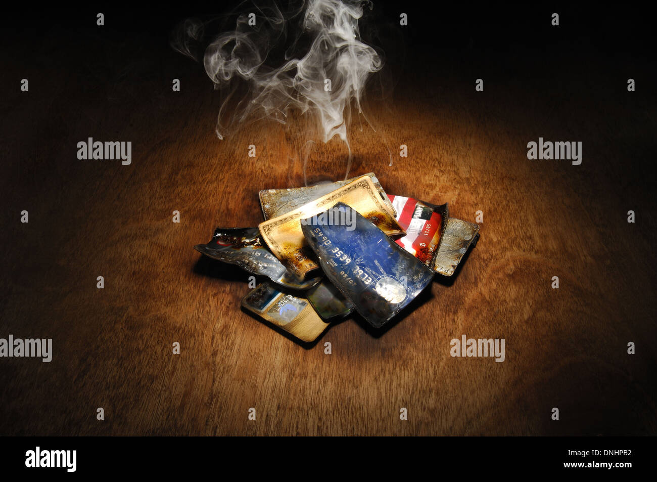 A pile of burnt credit cards with trails of smoke Stock Photo