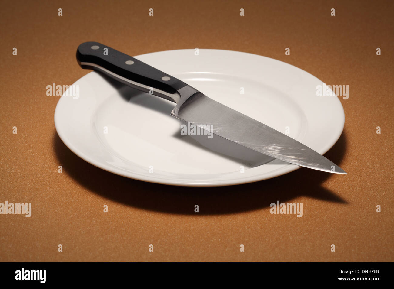 A large kitchen chef's knife on a empty white dinning plate. Stock Photo