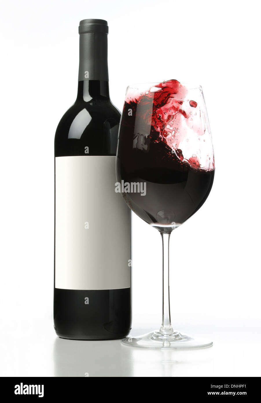 A bottle of red wine with a splashing glass of red wine. Stock Photo