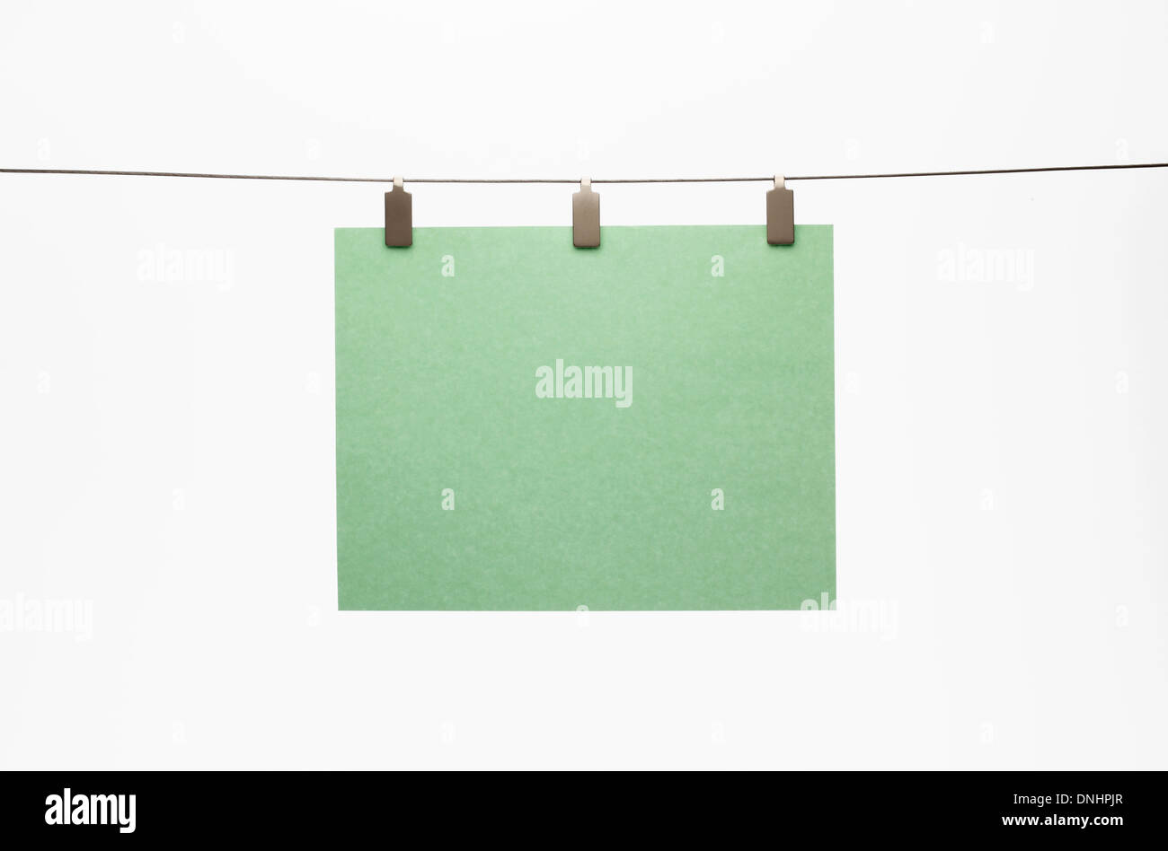 A blank piece of green paper hanging with a clip to a straight wire. White background Stock Photo