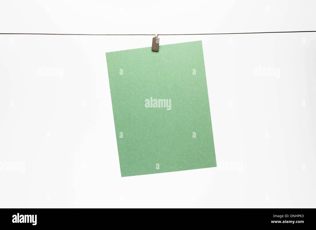 A blank piece of green paper hanging with a clip to a straight wire. White background Stock Photo