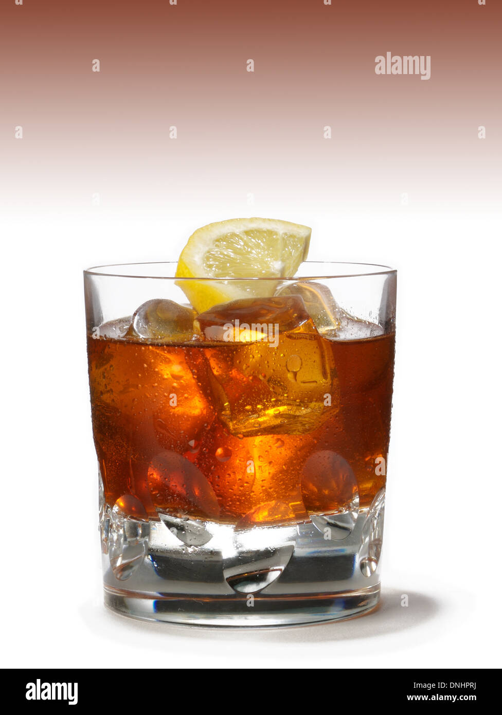 A low ball glass with bourbon over ice with a lemon wedge as garnish. Stock Photo