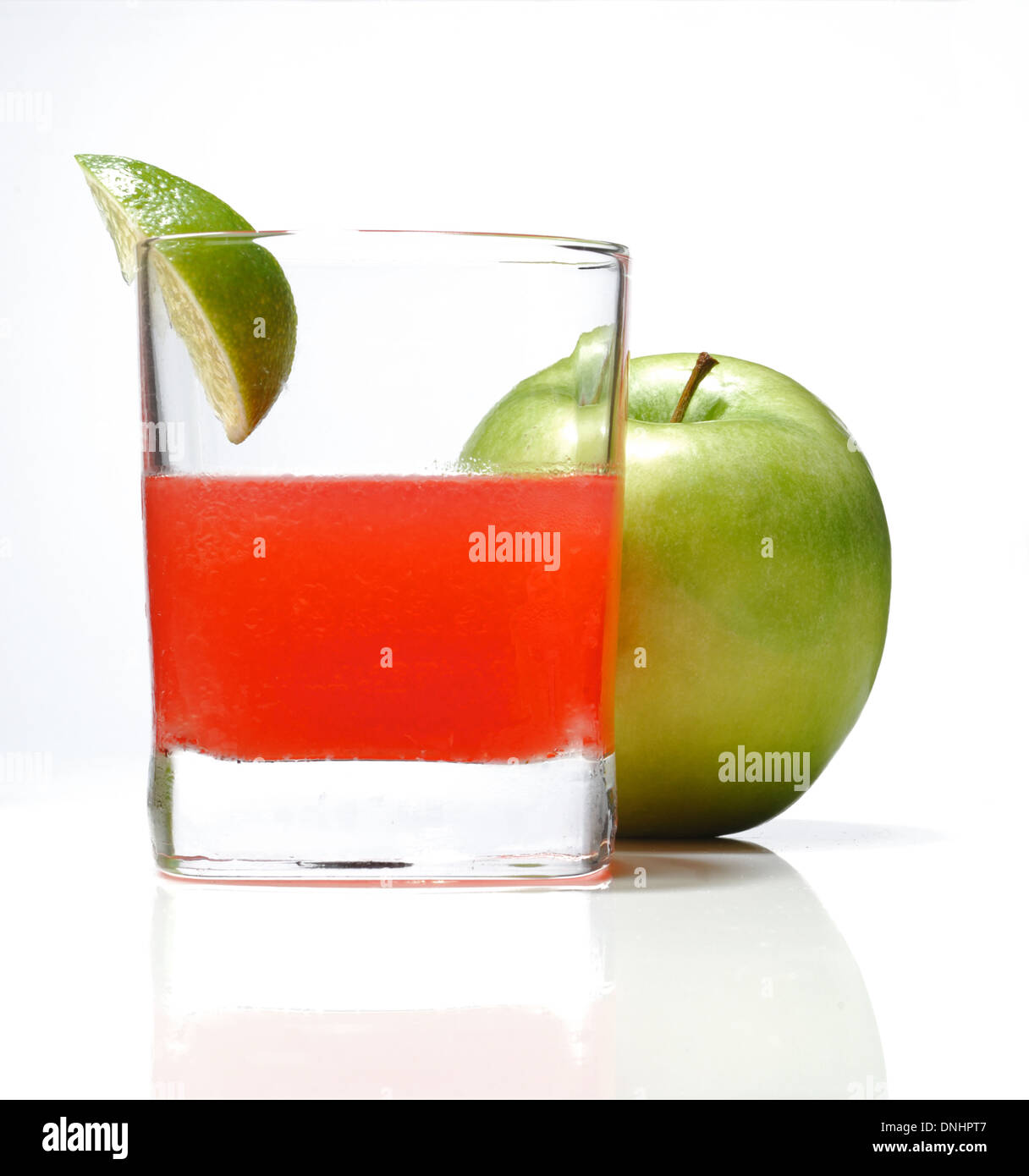 A colorful cocktail drink in a glass with a wedge of lime and a whole green apple. Stock Photo