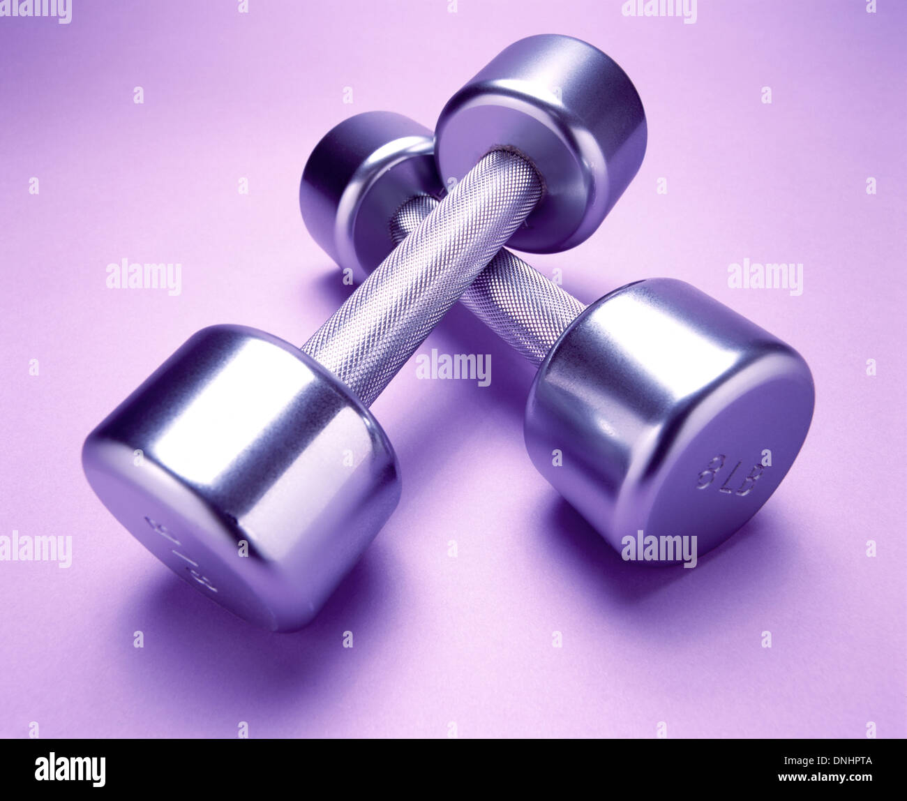 A pair of exercise metal free weights on a light purple exercise mat. Stock Photo