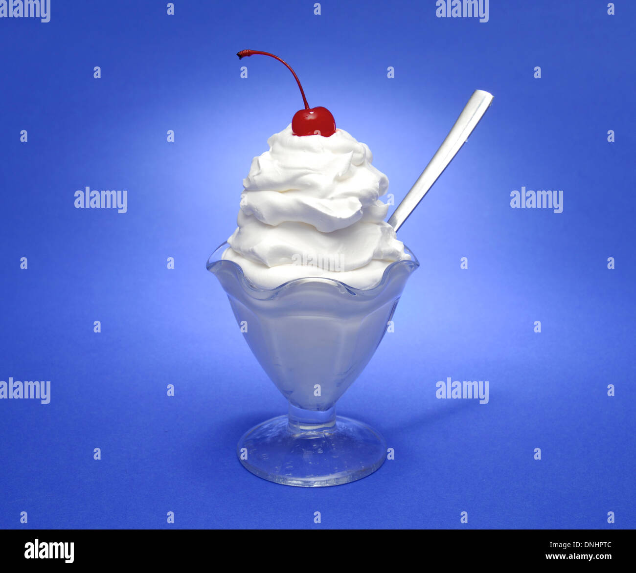 A white cream sundae dessert glass with a spoon and a red cherry on top